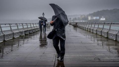man holding an umbrella trying to shelter from heavy rain and breezy weather
