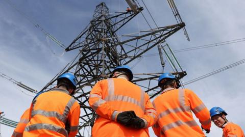 Workers in orange jackets with electricity pylon in front of them