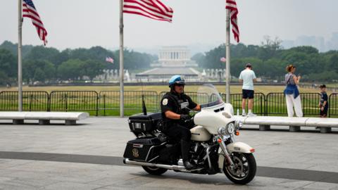 A US Park Police officer sits on a motorbike in front of the Washington Monument, with American flags in the background