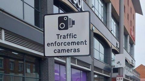 A sign for a traffic enforcement camera by a road. 