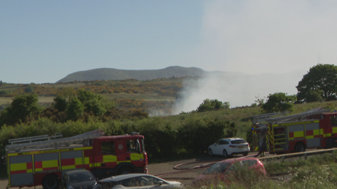 Two fire engines are pictured at the scene of the fire with smoke billowing over the hills