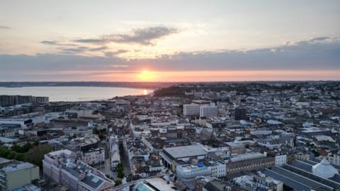 A drone shot above St Helier as the sun sets into the sea beyond.