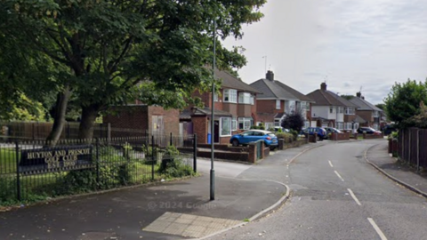 A street view of Fairway road. On the left side is a black fence with a sign reading 'Huyton and Prescot Golf Club'.