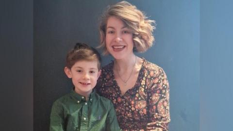 Bertie has brown hair and is wearing a green shirt. He is sitting with his mum Lauren, who has light brown short hair and is wearing a red and orange floral shirt.