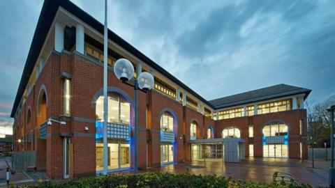 Reading Borough Council's offices - a red brick building with several large arched windows that are glowing from the inside light. It sits beneath a cloudy sky.