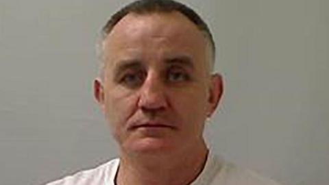 James Meehan is seen in a police stock photo wearing a white shirt. 
He has grey and black hair.
