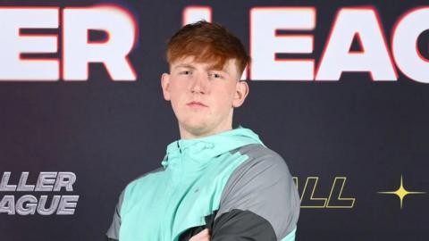 YouTuber Angry Ginge stands in front of a Baller League board.