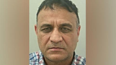 Muhammad Zahid's mugshot. He has short dark hair and is wearing a grey and red checked shirt