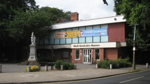 The outside of North Lincolnshire Museum with banners across the upstairs windows and a war memorial in the square outside