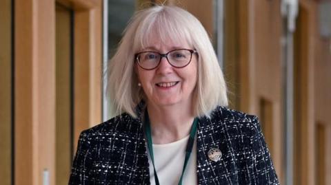 MSP Beatrice Wishart wearing glasses and smiling at camera as she walks along a corridor.