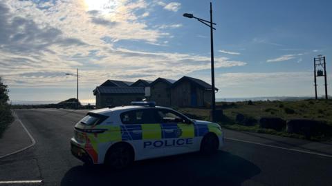 A police car at the scene by Crimdon beach. The car is parked across a road, blocking access.