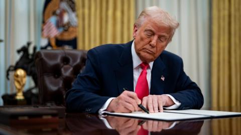 Donald Trump signs paperwork in the Oval Office in the White House