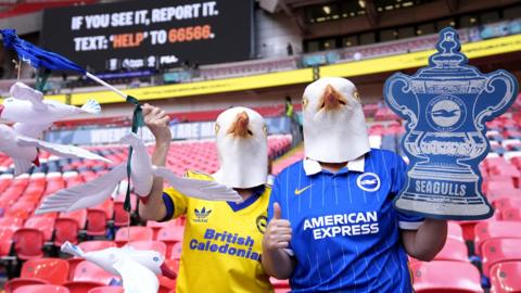 Two Brighton supporters with Seagulls masks clutching a cardboard FA Cup