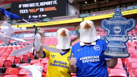 Two Brighton supporters with Seagulls masks clutching a cardboard FA Cup