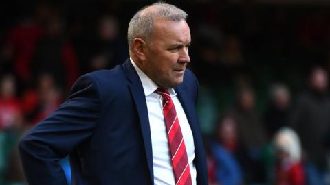 Wayne Pivac wearing white shirt, striped red tie and blue blazer in front of stadium crowd