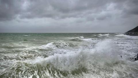 rough seas showing spray from large waves under a grey, cloudy sky