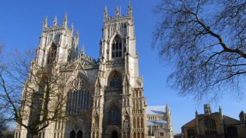 The 15th-century, gothic-style western towers of York Minster under a clear blue sky.