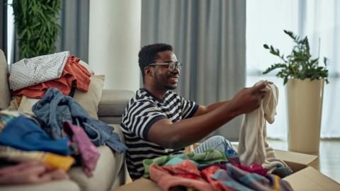 Young man putting clothes into a donation box at home - stock photo