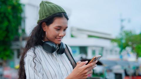 Woman using mobile phone. She is wearing a striped black and white shirt and a green beanie hat which covers her long, curly hair