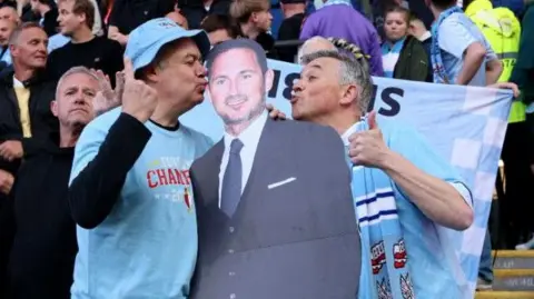 Two Coventry City fans kiss a cardboard cut-out of Frank Lampard 