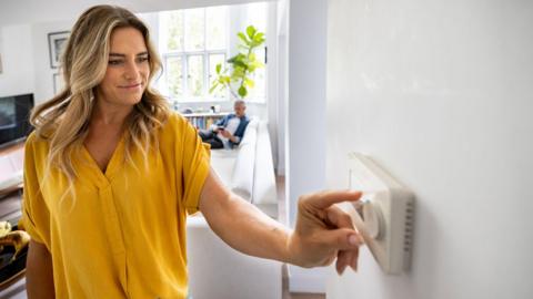 A blonde woman adjusts the temperature of her house with a dimmer - stock photo