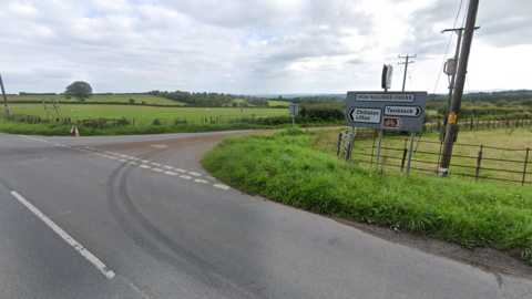 A rural road junction in Devon. Fields either side. A sign reads Iron Railings Cross. Other signs points to Chillaton Lifton and Tavistock.