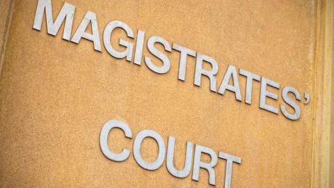 A large shiny metal sign on a brown wall which reads Magistrates Court