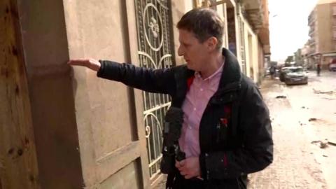 Nicky Schiller pointing at a water mark high on a wall, in the background the street is filled with mud 