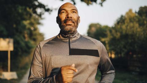 Close up of a middle-aged man walking quickly. He is wearing a grey exercise top.