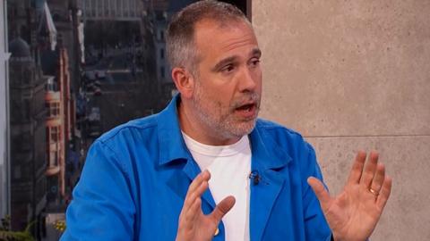 Dr Xand explaining the truth about testosterone supplements on Morning Live. Wearing a white shift with a blue shirt over the top.