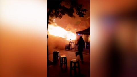 A person runs as fire spills out of the entrance to a bar