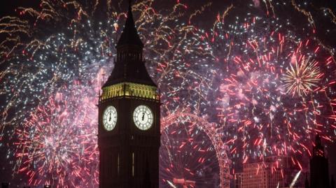 Big Ben in Westminster at night with New Year's Eve's colourful fireworks going off in the sky behind it. The London Eye can also be seen behind Big Ben.