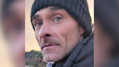 Missing man Jason. He is wearing a dark looking woolly hat and is looking at the camera. He has grey stubble and is wearing a dark coat.