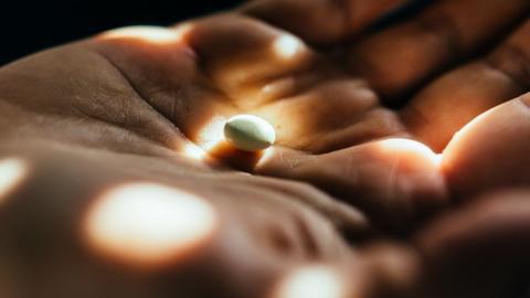 A hand holds a small pill in the palm. There is light reflecting off the hand in patterns.