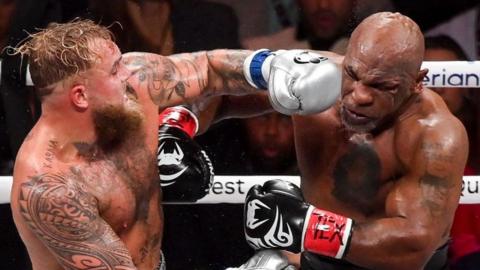 Jake Paul, to the left of the frame, lands a punch on Mike Tyson during their so-called boxing match. The event was Netflix's first foray into live boxing. Paul is wearing sliver gloves and Tyson's gloves are black with white markings on them, similar to his infamous 'tribal' facial tattoo.