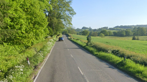 A rural road with trees to one side and a vista across fields to the other