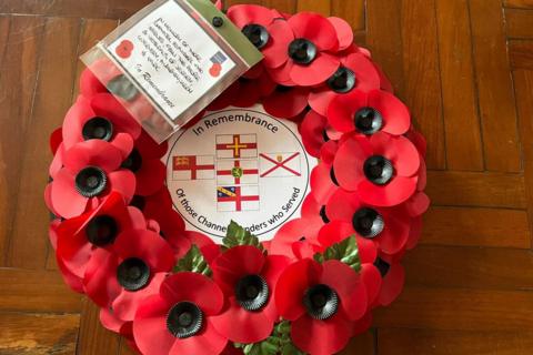A wreath of plastic red poppies. In the middle it says 'In Remembrance of those Channel Islanders who served'. It has the flags of Guernsey, Jersey, Alderney, Sark and Herm