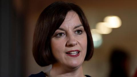 Bridget Phillipson has a dark brown bob hair do as she speaks to members of the press with a neutral expression 