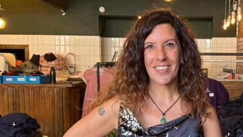 Cristina is smiling at the camera, in the background are different coloured school jumpers.