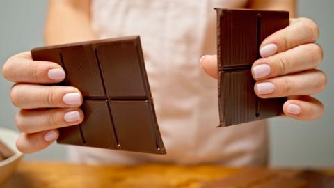 Hands break a large bar of dark chocolate in two.