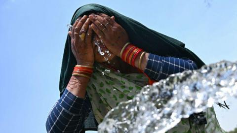 A woman washes her face with water to cool off during a hot summer day near the India Gate in New Delhi