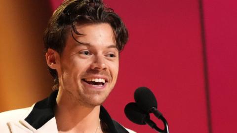 Harry Styles accepts Album Of The Year for Harry's House onstage during the 65th Grammy Awards in Los Angeles. He is smiling and is wearing a cream suit jacket with black velvet lapels.