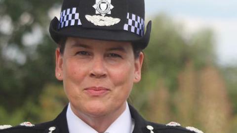 Assistant Commissioner Pippa Mills wearing the uniform of the Met Police, including epaulettes and a hat. She has a small stud earring in each ear and her hair is tucked away. She looks at the camera and has a pleased expression.