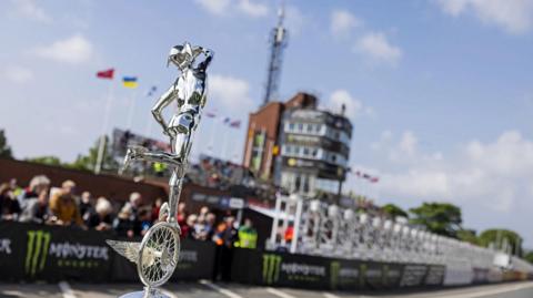 A silver TT trophy in front of the grandstand.