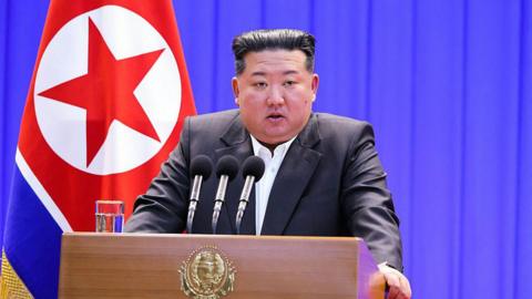 Kim Jong-un stands behind a podium, with the North Korean flag behind him