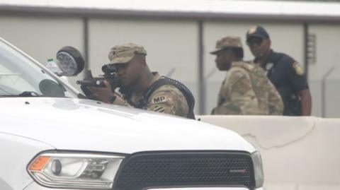 A soldier points a rifle over the bonnet of a white vehicle