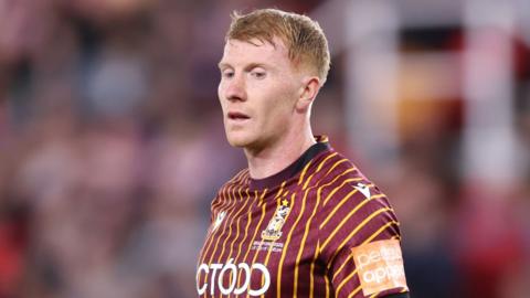Brad Halliday looks down to the ground and wears a claret and amber shirt.