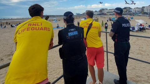 Two police officers and two RNLI lifeguards look out across a beach.