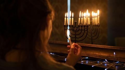 A young girl lighting candles with festive lights in front of her also.