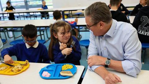 Britain's Prime Minister Keir Starmer (R) speaks with pupils over lunch during a visit to a primary school in Essex, eastern England, on June 5, 2025. The UK Government announced Thursday that over half a million more children are to get free school meals.
